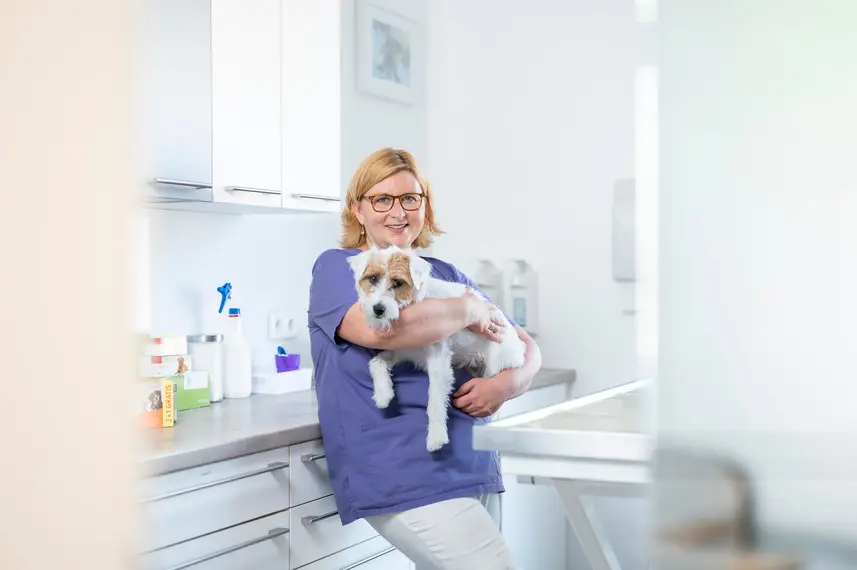 Tierärztin hält Hund im Arm und lächelt